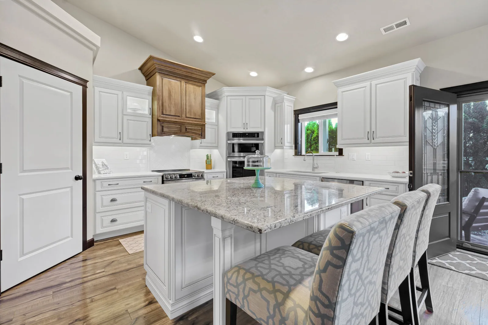 Kitchen with granite island, white cabinetry and wood hood