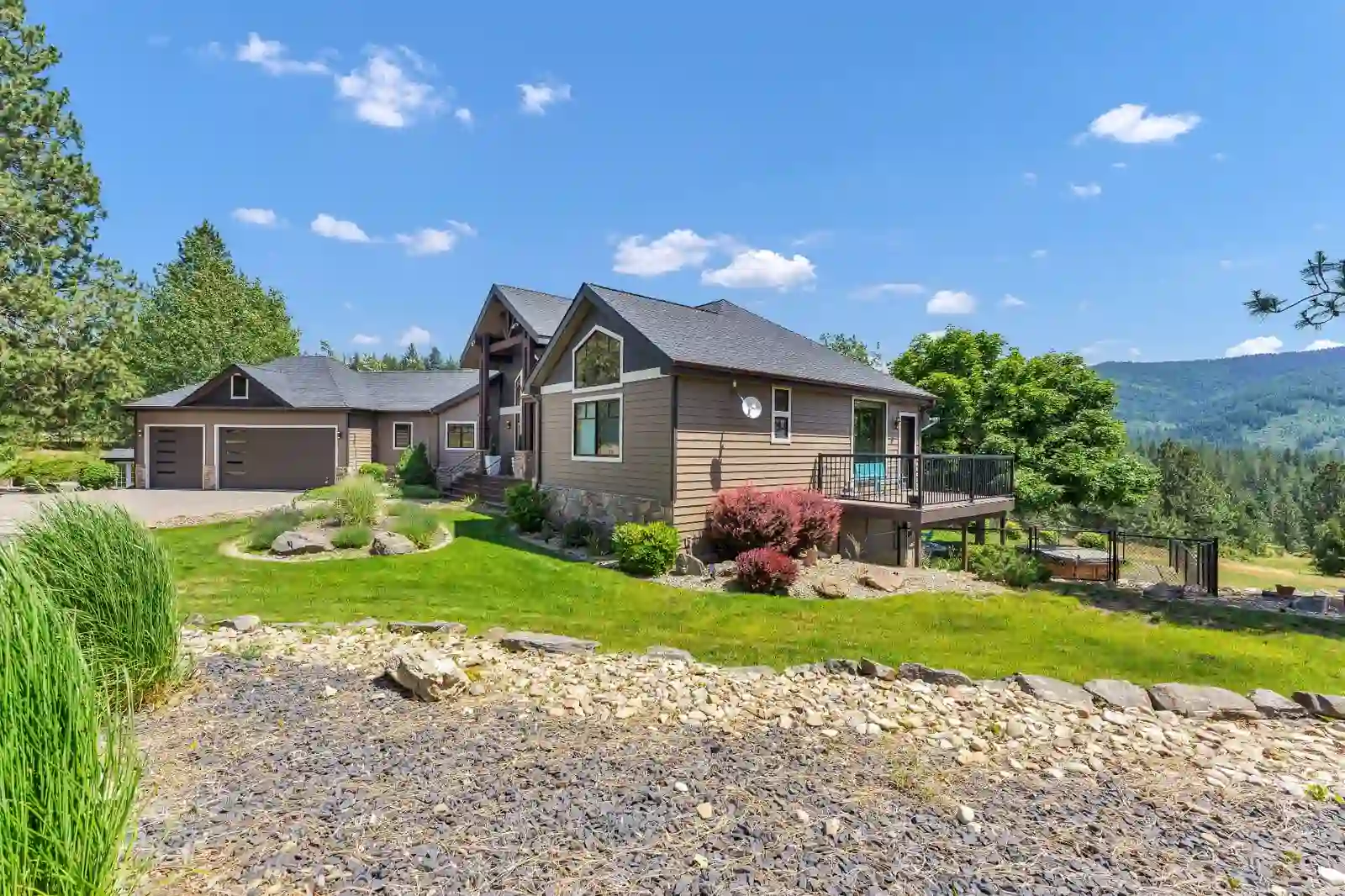 Ground-level exterior of the home with deck, landscaped yard and forested mountain backdrop