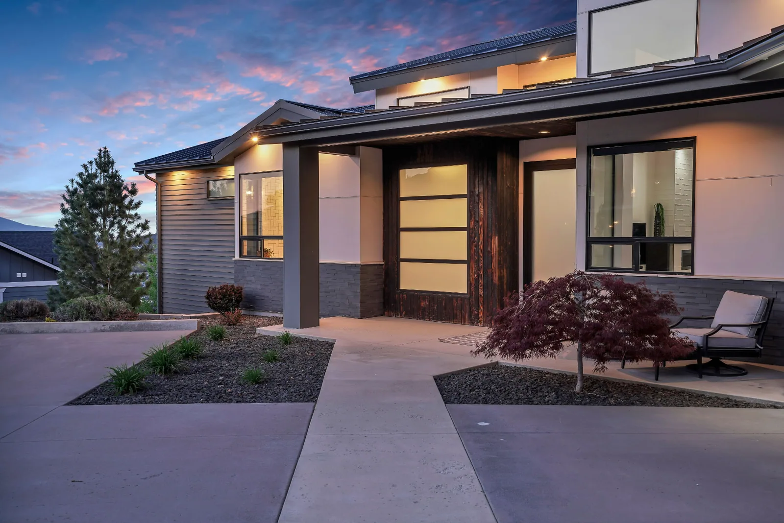 Covered entry with wood cladding and frosted glass door under a sunset sky