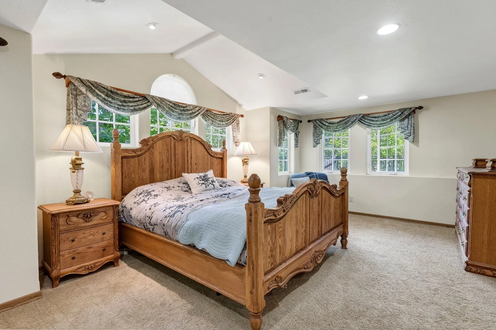 Bedroom with vaulted ceiling, carved oak bed and windows overlooking the treetops