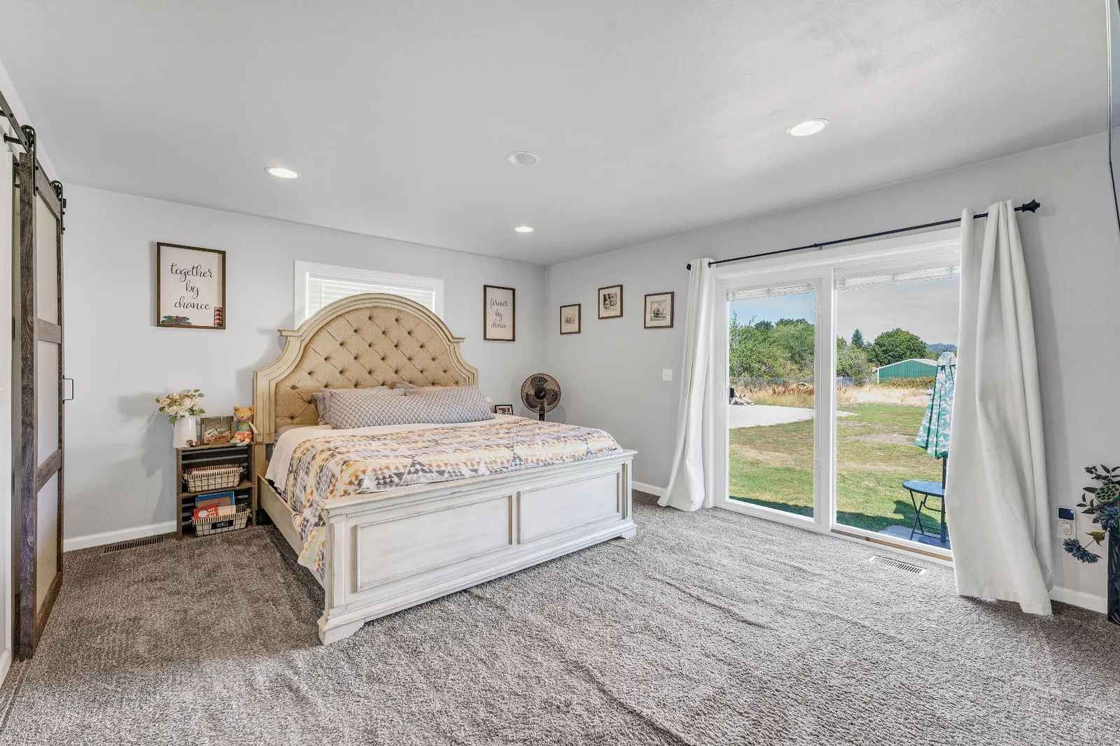 Primary bedroom with barn door, plush carpet and sliding doors to the backyard