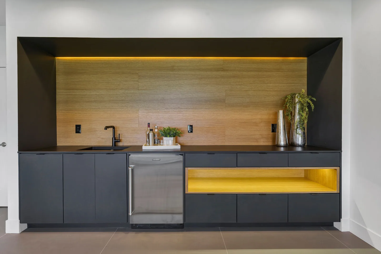 Wet bar with matte black cabinetry, oak backsplash and integrated lighting