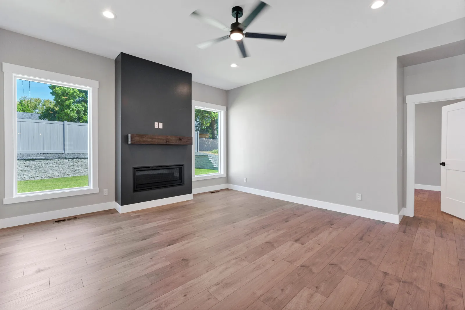 Living room with linear fireplace, wood mantel and windows to the backyard