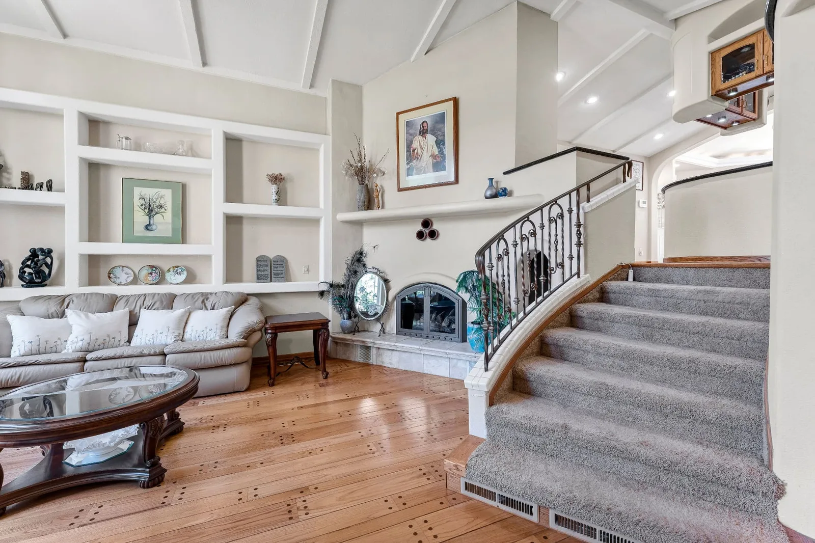 Living room with vaulted beamed ceiling, built-in shelving, fireplace and curved wrought-iron staircase