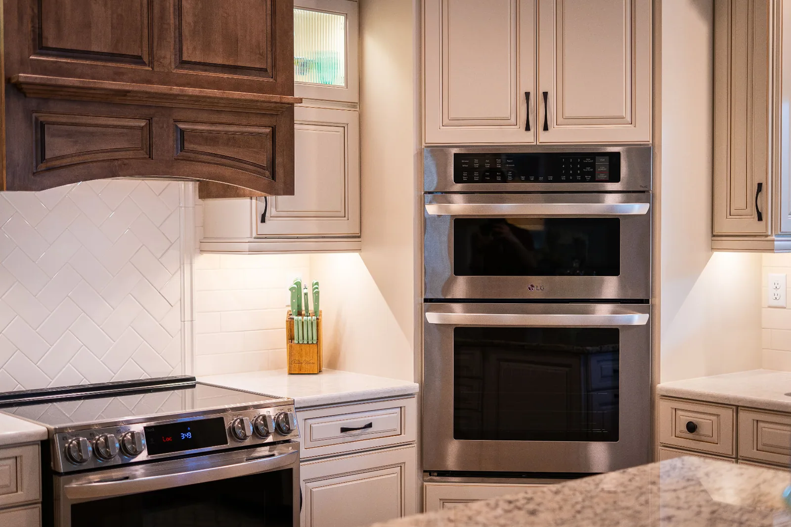 Range, double wall ovens and glazed cabinetry with herringbone tile