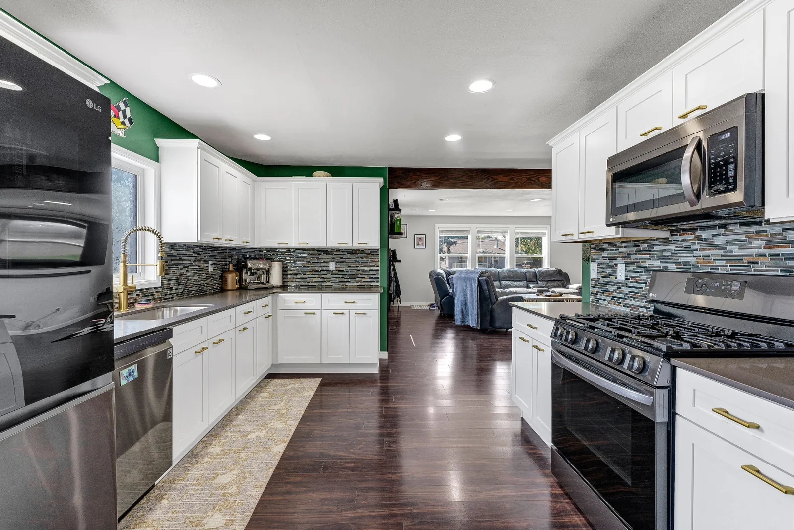 Kitchen with white shaker cabinetry, gas range and glass tile backsplash open to the living room