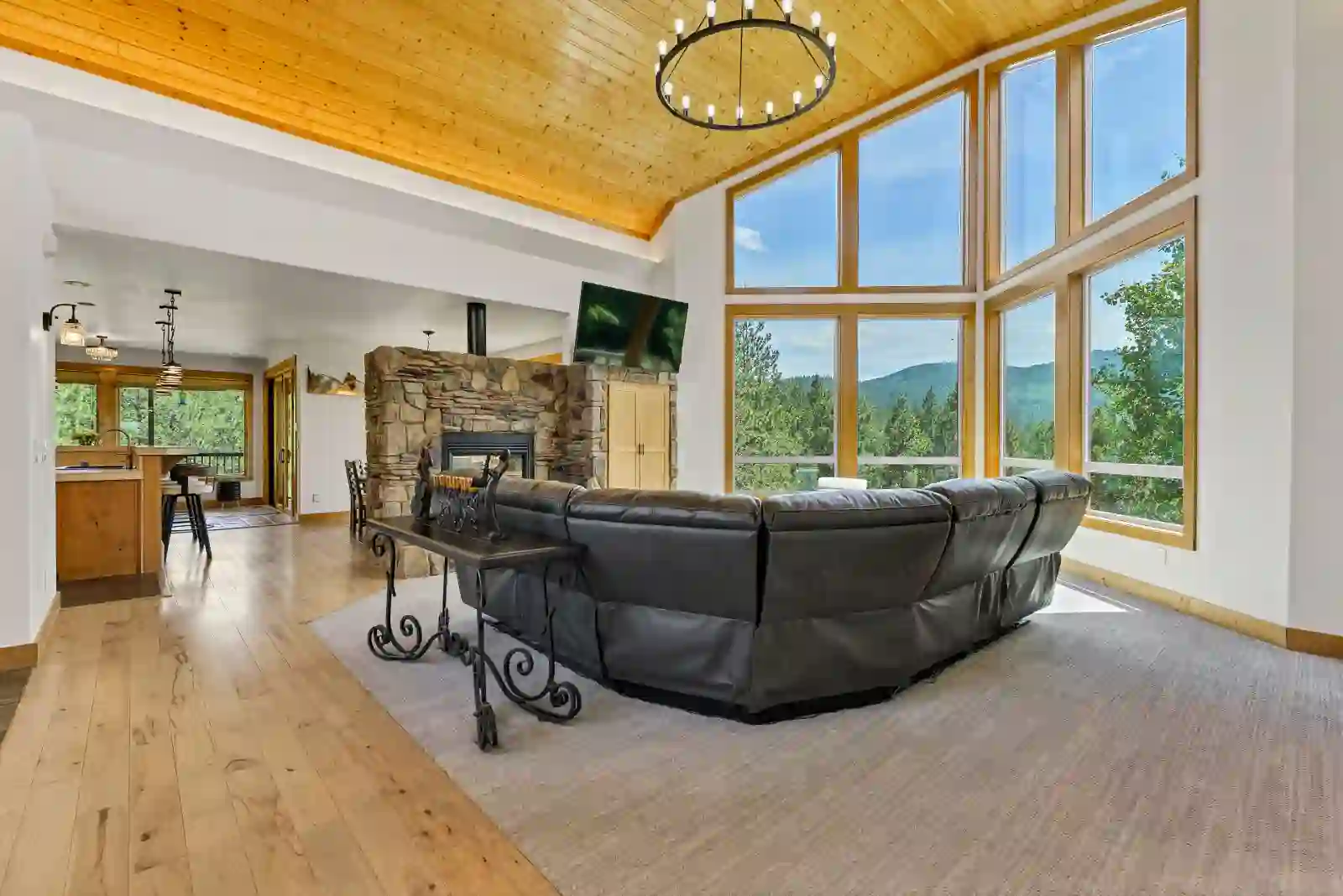Wide view of the great room's window wall, vaulted wood ceiling and open kitchen beyond