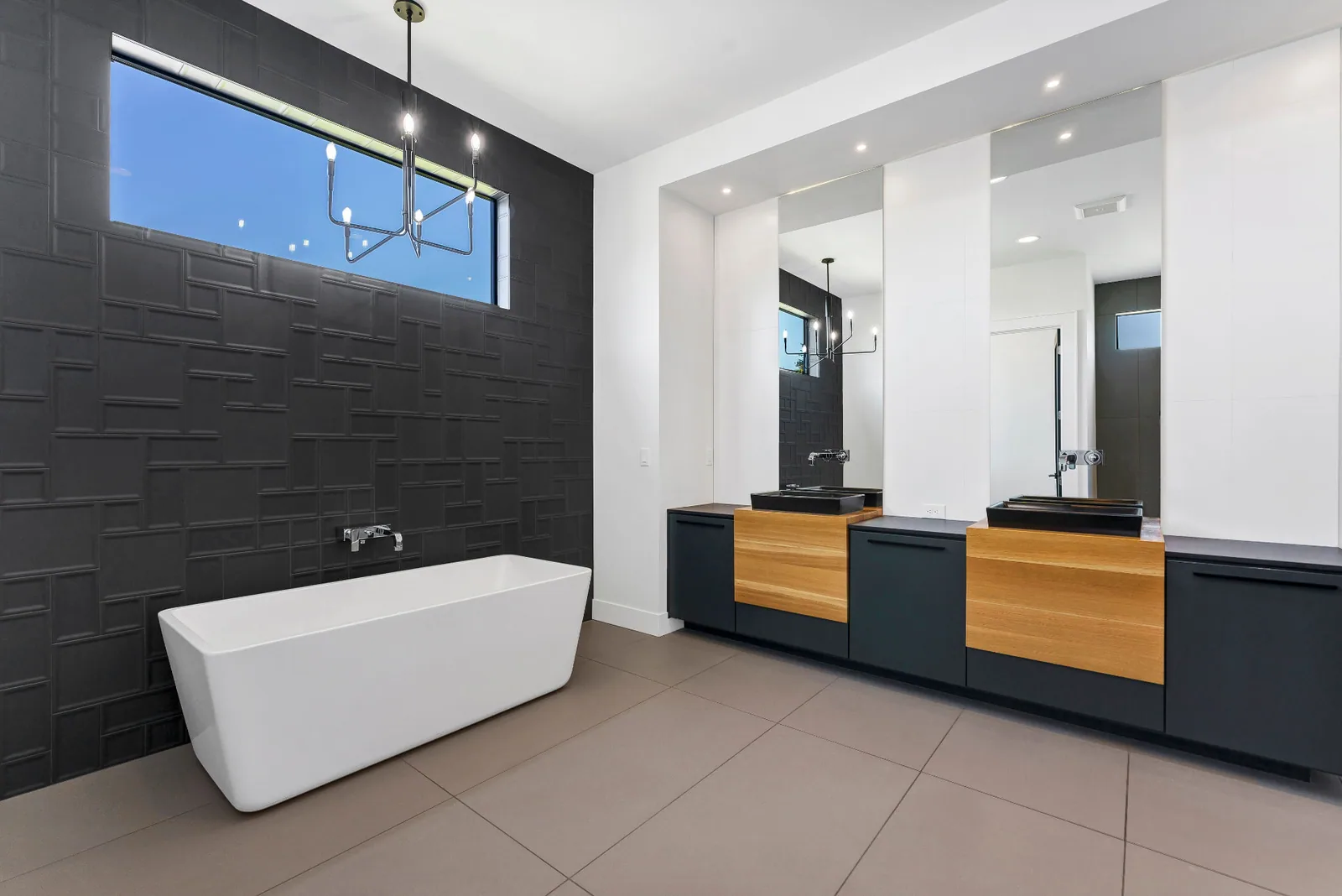 Primary bath with freestanding tub, textured black tile wall and double floating vanities