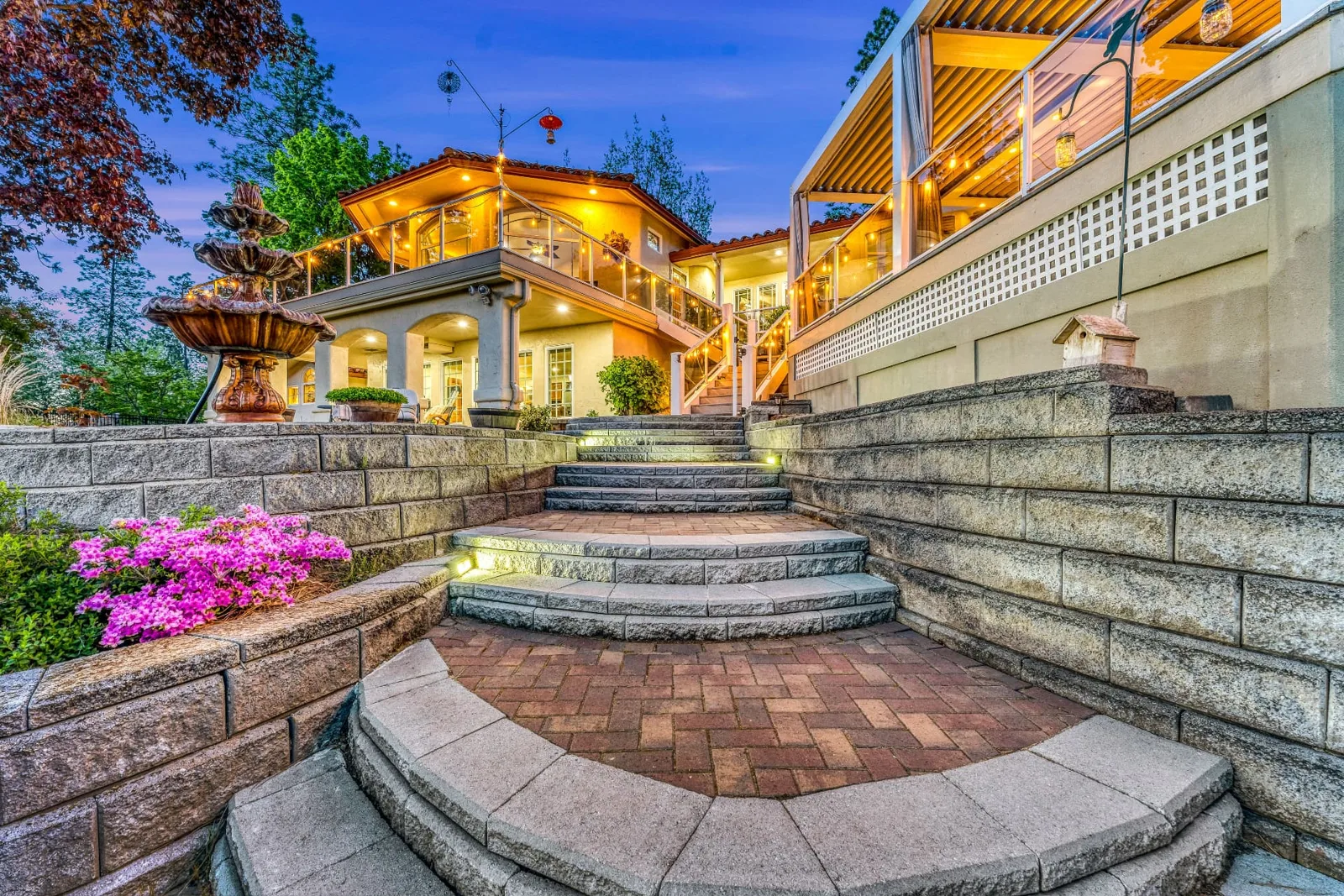 Lit stone terrace steps rising to the glowing twilight home and fountain