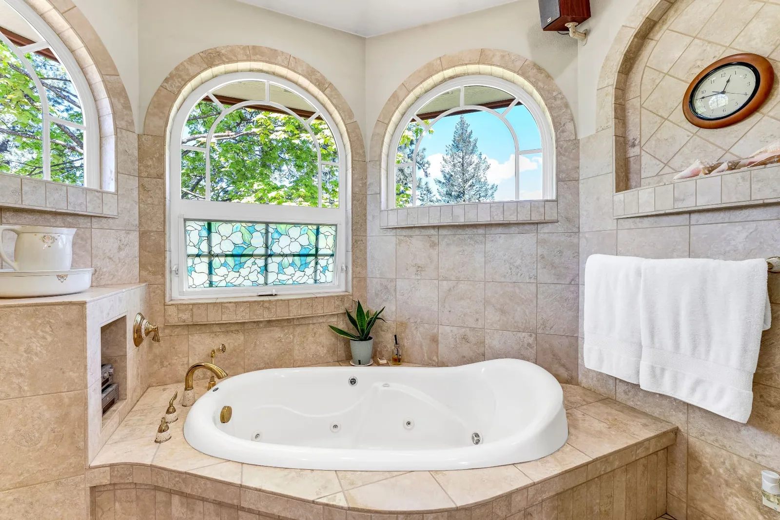 Tiled bath with corner jetted tub set beneath three arched windows