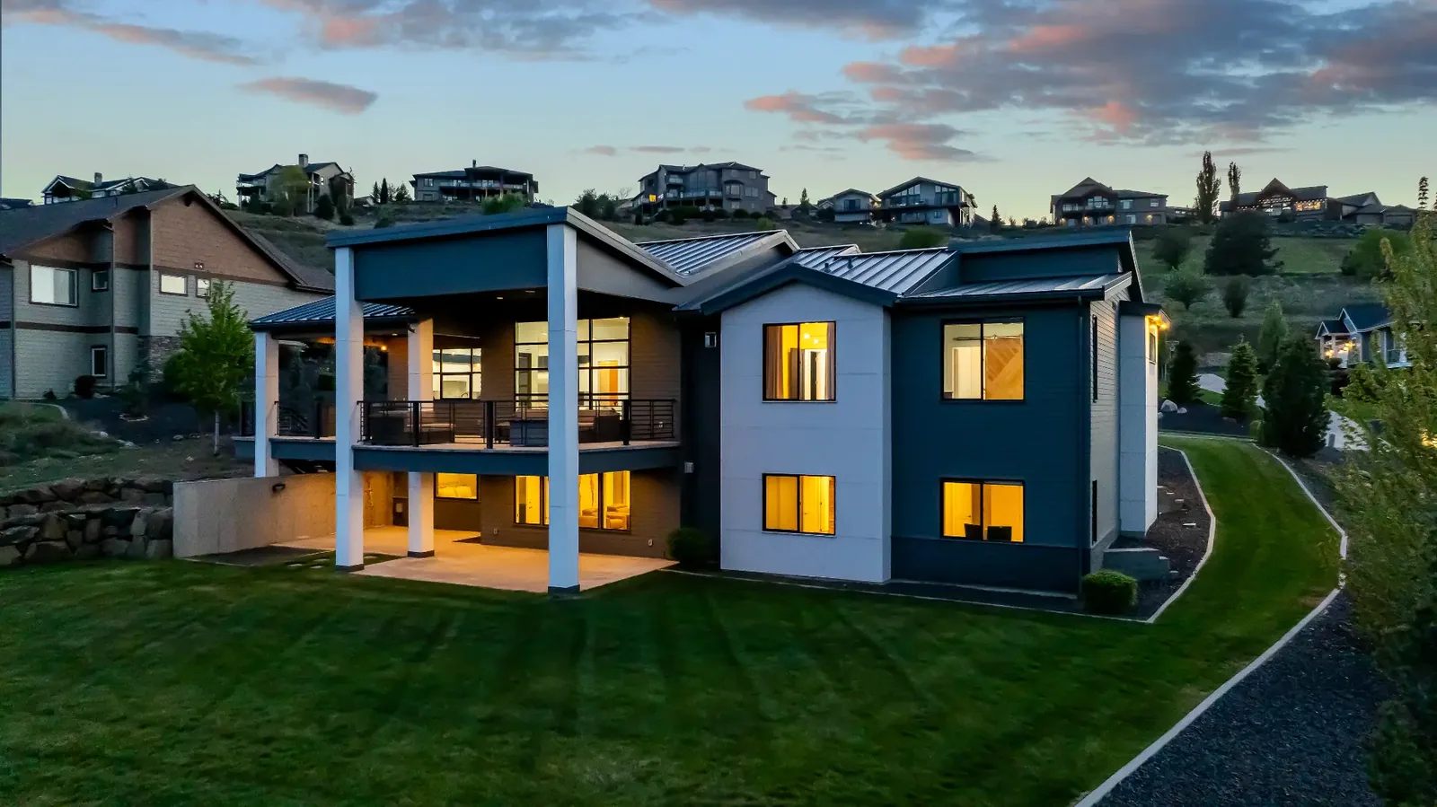 Rear elevation at twilight with covered deck, lower patio and lawn